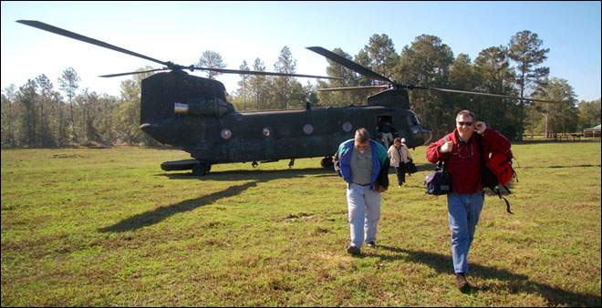 A U.S. Army Chinook helicopter from the Alabama National Guard lands in a cow pasture after an in-flight emergency forced it down. Members of the media walk away as the crew shuts it down to make repairs.