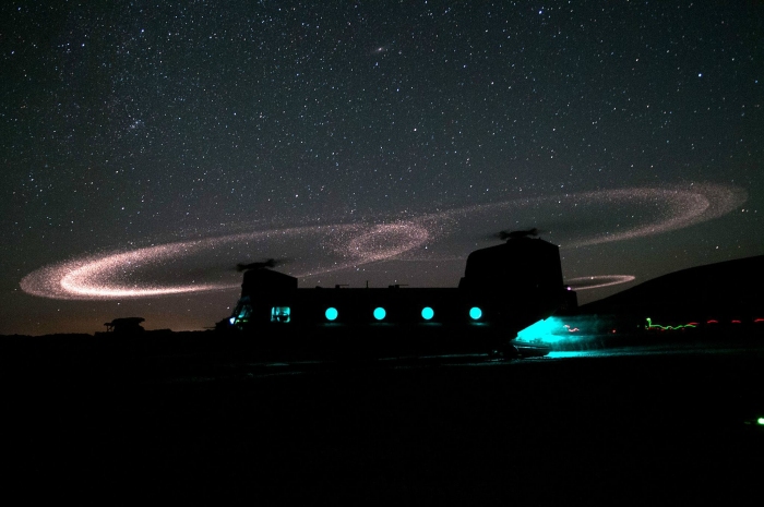 An unknown H-47 Chinook helicopter glows in the dark underneath a starry sky.
