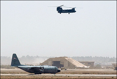 A United States operated C-130 - " Hercules" cargo plane lands as a U.S. Army CH-47D Chinook helicopter flys overhead at Baghdad International Airport.