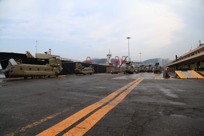 3 November 2013: On a cold and rainy November morning Boeing Maintenance crews work diligently to assemble the CH-47F Chinook helicopter fleet while the aircrews perform final airworthiness inspections prior to departing for Camp Humphreys, Republic of Korea. In the background sits the transport vessel "Lightning" in which the fleet and ground simulators arrived.
