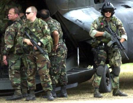 Two U.S. Special Forces stand guard with their firearms as other members board a U.S. MH-47E in the Philippines.