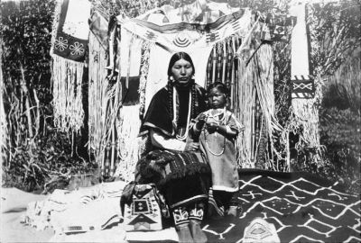 Cayuse/Chinook woman known as Ida Howlish or Te-Mow-E-Ne poses with child and many beaded objects.