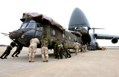 Army and Air Force personnel utilize their brute strength to load two CH-47D Chinook Army helicopters onto a C-5A Galaxy.